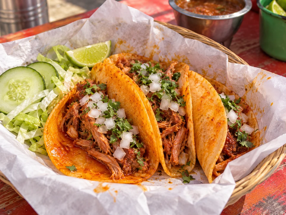 Soft red chile-stained corn tacos filled with shredded pork in a basket.