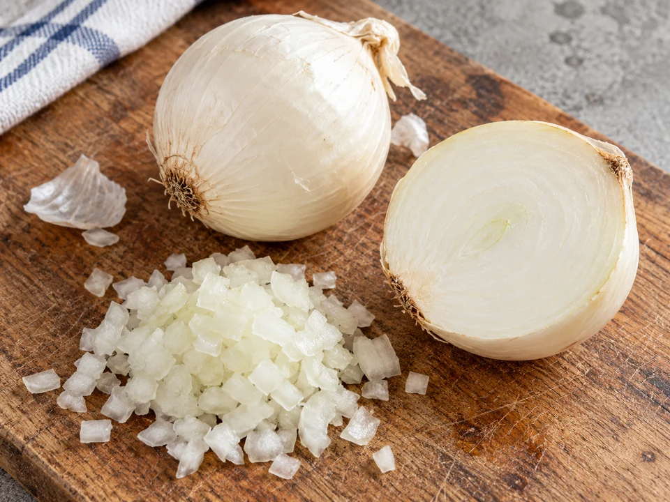A whole white onion, a halved white onion and finely diced onion on a board.